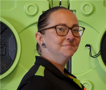 Smiling woman with glasses in SERVPRO uniform standing in front of green equipment