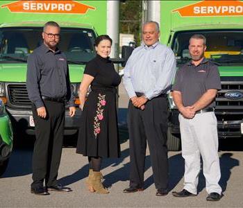Smiling team, one women and three men, standing in front of SERVPRO Trucks