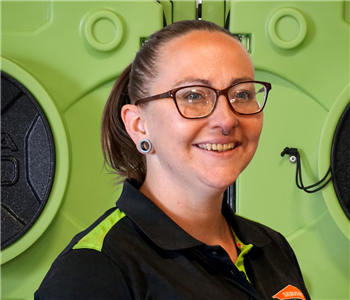 Smiling woman with glasses in SERVPRO uniform standing in front of green equipment