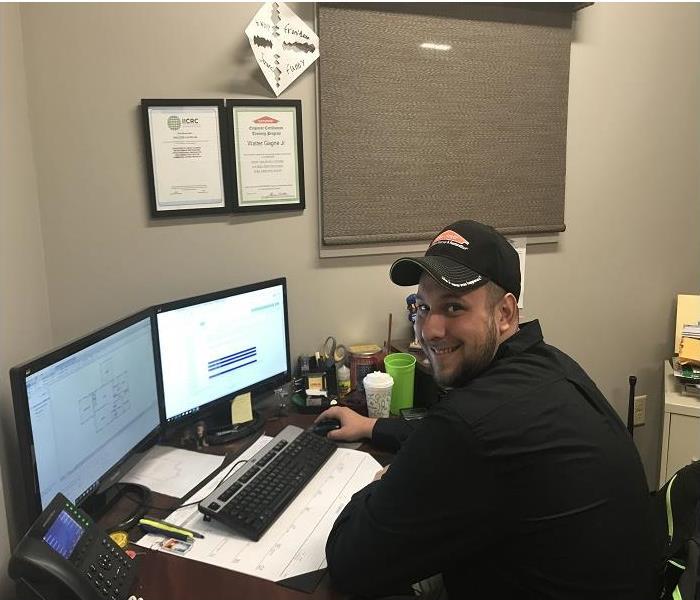 Smiling man, working at computer in SERVPRO uniform and hat
