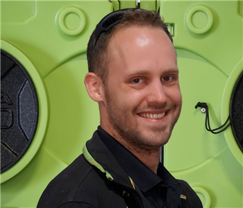 Smiling man with beard, in SERVPRO uniform in front of green equipment