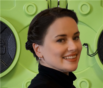 Smiling dark haired woman inblack dress in front of green equipment